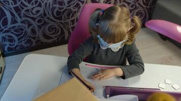 Child girl in medical mask doing school homework, using laptop computer at home. Back to school, online learning, distance lesson, kid pupil education at home, technology for schoolgirl. Slow motion video