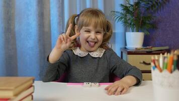 Child girl looking at web camera making call, learning, studying lessons at home, smiling, showing tongue. Online pupil distance internet education for children kids on coronavirus lockdown video