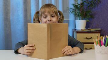 Child girl looking at web camera making call learning, studying lessons at home, reading book, smiling. Online pupil distance internet education lesson for children kids on coronavirus lockdown video