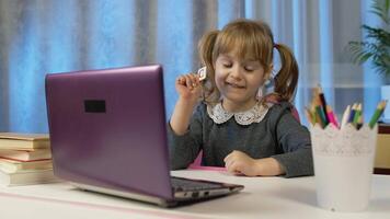 Child girl doing school homework, writes in notebook, using laptop computer at home. Back to school, online learning, distance lesson, pupil education at home, technology for schoolgirl. Slow motion video