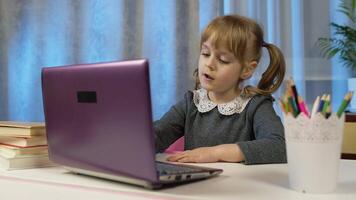 Child schoolgirl learning lessons being at home sitting at table using laptop digital computer. Portrait of kid girl distance education. Studying during coronavirus lockdown. Slow motion. 6k downscale video