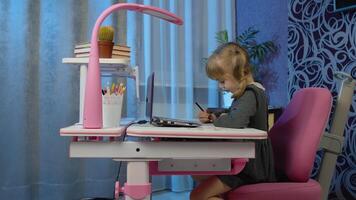 Child schoolgirl learns lessons with teacher being at home sitting at table using digital laptop computer. Portrait of a kid pupil girl distance education. Studying on coronavirus quarantine lockdown video