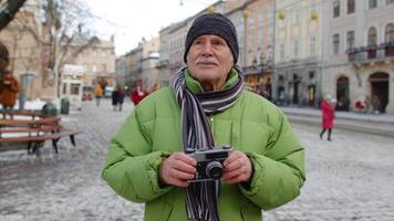 retrato de mayor hombre tomando imágenes con foto cámara, sonriente utilizando retro dispositivo al aire libre en invierno ciudad centrar de lviv, Ucrania. fotografía, de viaje, vacaciones. activo vida después Jubilación video