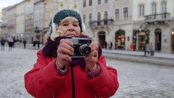 retrato de mayor mujer turista tomando imágenes con foto cámara, utilizando retro dispositivo al aire libre en invierno ciudad centrar de lviv, Ucrania. fotografía, de viaje, vacaciones. activo vida después Jubilación video
