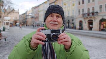 retrato de mayor hombre tomando imágenes con foto cámara, mirando a cámara utilizando retro dispositivo al aire libre en invierno ciudad centrar de lviv, Ucrania. fotografía, de viaje, vacaciones. activo pensionista video