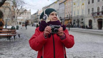 mayor mujer abuela turista tomando imágenes con foto cámara, sonriente utilizando retro dispositivo al aire libre en invierno ciudad centrar de lviv, Ucrania. fotografía, de viaje, vacaciones, viaje, Navidad víspera video