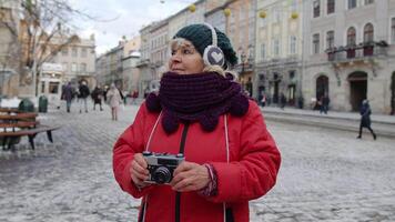 mayor mujer turista tomando imágenes con foto cámara, utilizando retro dispositivo en invierno ciudad lviv, Ucrania. fotografía, de viaje, vacaciones. activo vida después Jubilación durante coronavirus encierro video