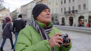 mayor hombre abuelo tomando imágenes con foto cámara, sonriente utilizando retro dispositivo al aire libre en invierno ciudad centrar de lviv, Ucrania. fotografía, de viaje, vacaciones, viaje, Navidad Días festivos víspera video