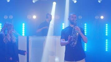 Musical band group playing song, performing on concert musician stage with lights. Singer vocalist girl, saxophonist sax, DJ man. Music actors dancing, singing at rehearsals preparing for performances video