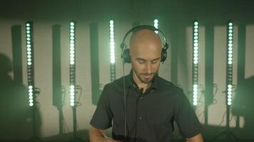 Live DJ performance of emotional energetic bald man with headphones. Party, music festival show concert. DJ composing new mix, dancing, performing on concert musician stage with lights. Slow motion video