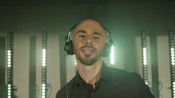 DJ composing new mix, dancing, performing on concert musician stage with lights. Party, music festival show concert. Live DJ performance of emotional energetic bald man with headphones. Slow motion video