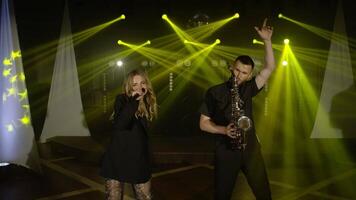 Musical band group playing song, performing on concert musician stage with lights. Singer vocalist girl, saxophonist sax man. Music actors dancing, singing at rehearsals preparing for performances video