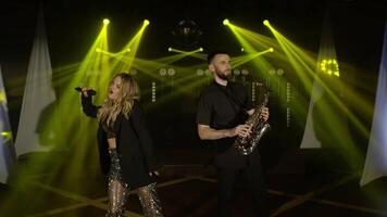 Musical band group playing song, performing on concert musician stage with lights. Singer vocalist girl, saxophonist sax man. Music actors dancing, singing at rehearsals preparing for performances video