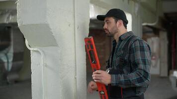 Man builder engineer checking wall with bubble level tool building construction electrician inspector foreman repairman guy male industry architect using instrument inspecting apartment renovation video
