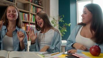 Funny carefree happy four teenagers dancing singing sitting table in school library classmates together dance at desk sing music listening enjoying preparing for exams education fun pupils pause learn video