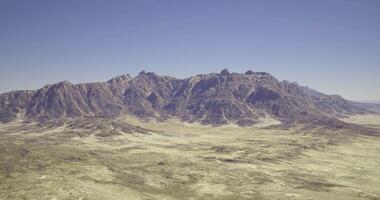 CGI Majestic mountain range rises above arid desert landscape under clear sky video