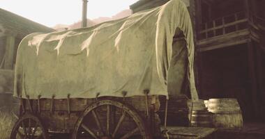 CGI Covered wagon stands in rustic setting near wooden structures video