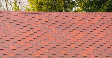 Asphalt shingles roofing construction waterproofing for new house, on the background of green trees. View on asphalt roofing shingles photo