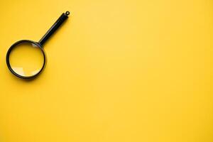 Top view of magnifying glass on yellow background, space for text. Search concept photo