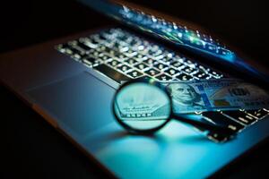 A laptop computer with a magnifying glass and a hundred dollars. Business concept. Soft focus photo