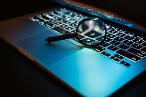 A magnifying glass is placed on a notebook computer. Search for viruses on a laptop computer photo