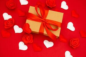 Valentine's Day. Gift box of kraft paper with a red ribbon. Red background with hearts and roses around photo