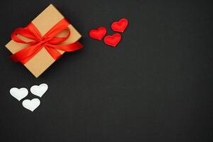Valentine day background with red hearts. Kraft Gift box with beautiful red ribbon. Top view red and white hearts on red background. Photo template, background