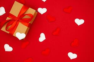 Valentine's Day background. Gift box of kraft paper with red bow on red background with hearts. Place for text, banner. photo
