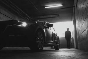 A man standing in front of a car in a dark garage photo