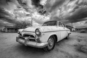 An old car sits in the desert under a cloudy sky photo