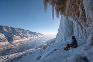 A man sitting on the edge of a cliff with ice formations photo