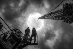 Two men standing on a construction platform looking at a crane photo