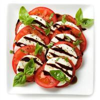 A classic Caprese salad with alternating slices of ripe tomatoes and fresh mozzarella, drizzled with balsamic glaze and olive oil. Fresh basil leaves add a pop of color and flavor, creating a simple yet elegant Italian dish. Isolated on clean white backgr photo