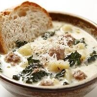 A close-up of a creamy zuppa toscana soup, a hearty Italian soup with sausage, kale, potatoes, and cream, simmered until thick and flavorful, garnished with grated parmesan cheese and crusty bread, served in a rustic bowl, isolated on clean white backgrou photo