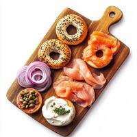 A wooden cutting board with an assortment of freshly baked bagels, served with cream cheese, smoked salmon, capers, and thinly sliced red onions. A classic breakfast option. Isolated on clean white background photo