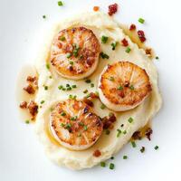 A plate of seared scallops with cauliflower puree, featuring tender seared scallops served over a smooth and creamy cauliflower puree, drizzled with a brown butter sauce and garnished with crispy pancetta crumbles and a sprinkle of chives, an elegant and photo