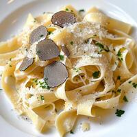 A plate of tagliatelle al tartufo estivo, featuring long, flat egg noodles, tossed in a creamy sauce, made with butter, parmesan cheese, and shaved summer truffles, resulting in a lighter yet flavorful version of the classic truffle pasta, garnished with photo