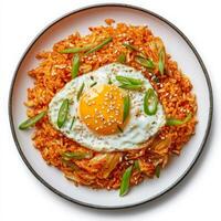 A plate of spicy kimchi fried rice, topped with a sunny-side-up egg and garnished with sesame seeds and sliced green onions. The dish has a vibrant red-orange hue, bursting with bold flavors. Isolated on clean white background photo