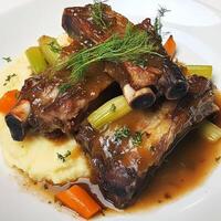A plate of braised pork ribs with white wine and fennel, featuring tender pork ribs, braised slowly in a white wine sauce with fennel seeds, onions, garlic, carrots, celery, and herbs, resulting in a harmonious balance of flavors and aromas, served with c photo