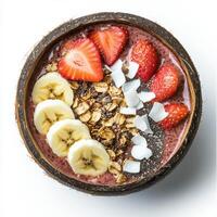 A vibrant smoothie bowl topped with sliced bananas, strawberries, shredded coconut, chia seeds, and granola, served in a coconut shell. A tropical and nutritious breakfast. Isolated on clean white background photo