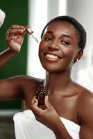 Woman applying facial serum while smiling in a serene bathroom setting during self-care routine photo
