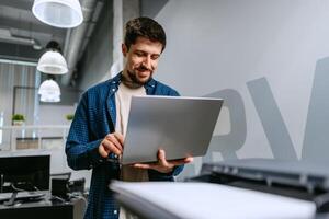 Man working on laptop in modern office environment during daytime with smiling expression photo