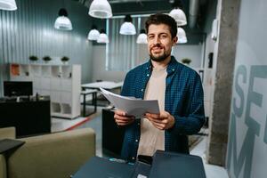 Office worker smiling while reviewing printed documents in a modern workspace during daylight hours photo