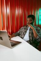 Young man working on laptop in modern workspace with vibrant red background during the day photo
