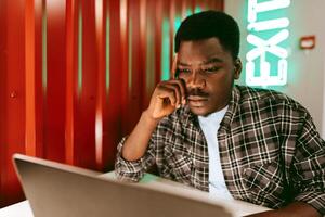 Focused individual analyzes data on laptop in a modern workspace illuminated by neon lights in the evening photo