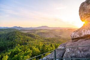 The Lusatian Mountains offer a breathtaking view from Popov Cliffs during the evening. The sandstone formations shine under the soft glow of the sunset, creating a peaceful atmosphere. photo