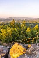 Visitors enjoy the breathtaking sunset from the lookout at Popov Cliffs in the Lusatian Mountains, surrounded by lush greenery and sandstone rock formations. photo