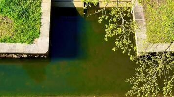 This aerial footage highlights a stone bridge over a serene river, surrounded by lush greenery. Sunlight creates a rainbow effect on the water photo