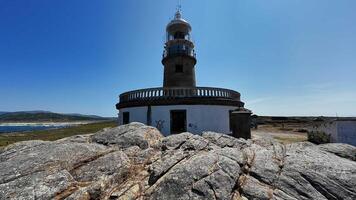 A picturesque scenic view of a charming lighthouse surrounded by rugged rocky terrain and a clear blue sky photo