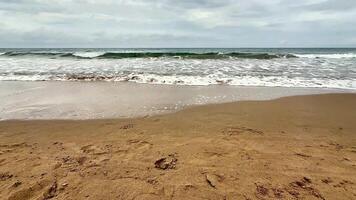 A tranquil and serene beach landscape featuring soft, golden sand, gentle waves, and overcast grey skies photo